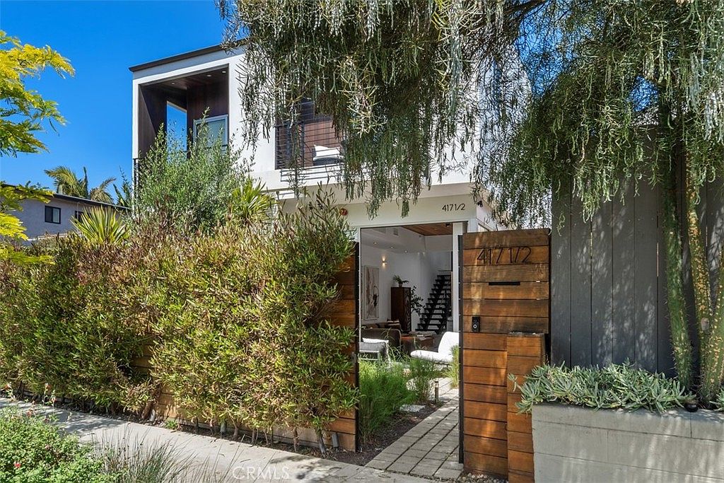 Front entry with wood gate, lush landscaping, and the modern facade beyond