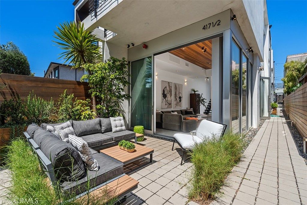 Modern Venice residence with retractable glass doors opening from the wood-beamed living room to a private patio with palm tree and lounge seating